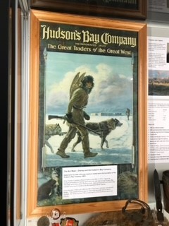 Hudson Bay recruitment poster on display at the Stromness Museum photograph of a framed poster in Stromness Museum. The poster is a recruitment poster depiicting a man walking through the snow dressed in skins and carrying snow shoes on his back. He carries a shotgun in his right hand. Two wolves/huskies accompany him.
