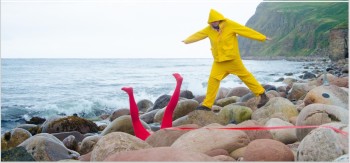 two figures on a beach, one is standing in a yellow outfit, and a second in lying down with their legs in the air wearing red tights.
