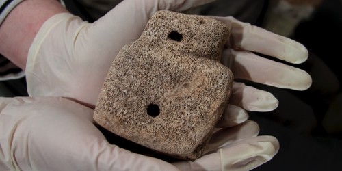 A carved whalebone figurine being held in a pair of gloved hands