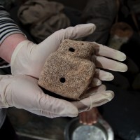 A carved whalebone figurine being held in a pair of gloved hands